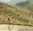 Девочка - китаянка, лет 10, в красных штанах, за спиной ранец, идет по тропинке на фоне рисовых террас деревни Баша, Гуйчжоу, Китай