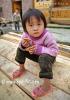 Китайское дитя в сиреневой кофточке, вельветовых брючках, пластиковых шлепанцах на босу ногу, браслетом на ноге, и с крекером в ручках