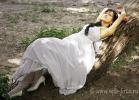 Невеста позирует фотографу, лежа на стволе дерева, растущего под наклоном к земле